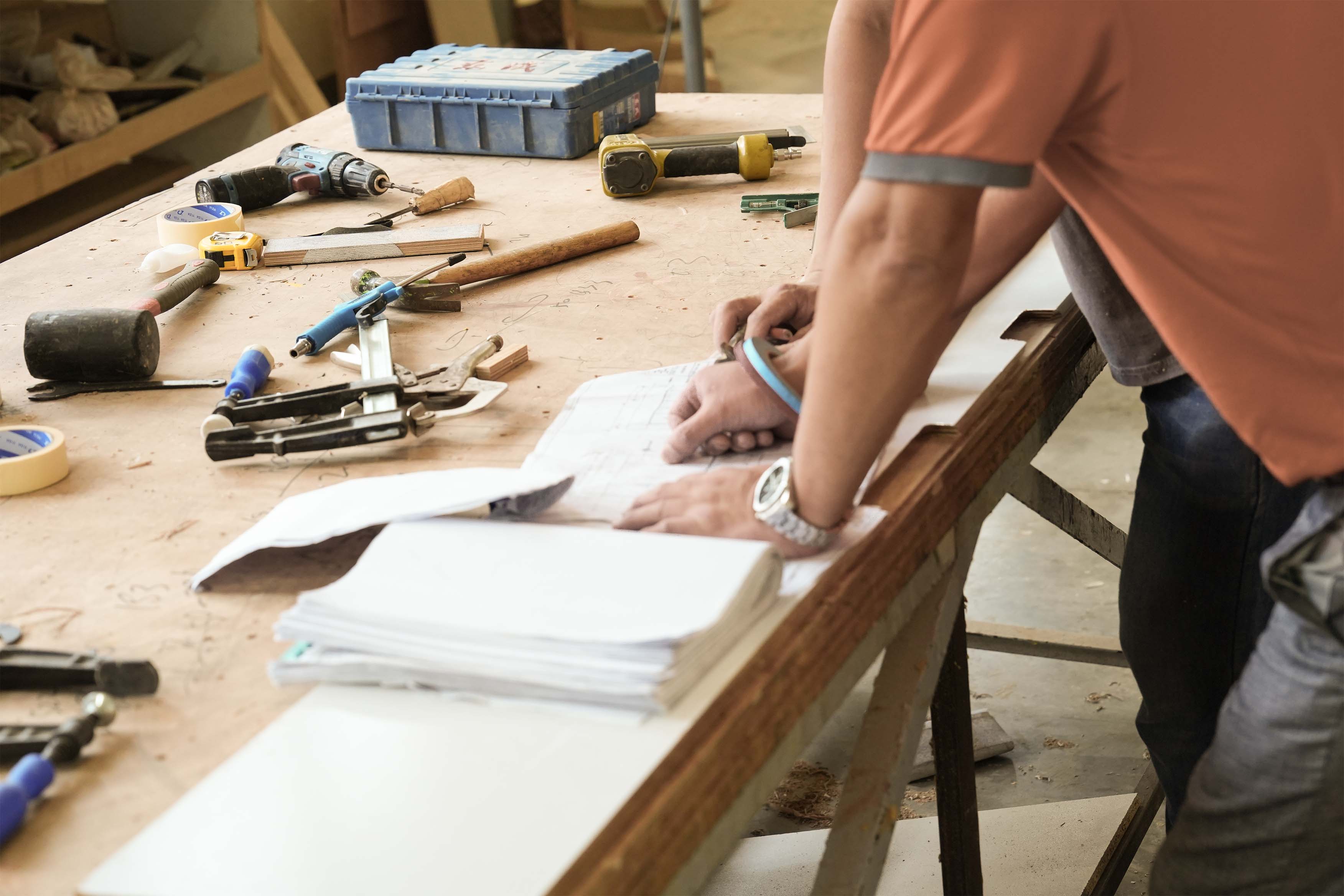 Furniture makers reviewing drawings beside tools on a workshop bench